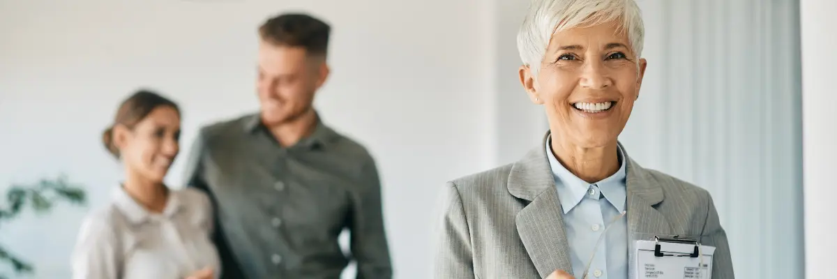 Corretora de imóveis com mais de 60 anos apresentando imóvel para jovem casal.