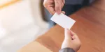 Corretor de imóveis entregando seu cartão de visitas físico para cliente em evento.