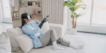 Mulher sentada em um sofá usando óculos de realidade virtual para ver decoração de imóvel.