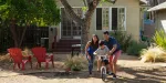 Família andando de bicicleta na frente da sua nova residência no exterior.